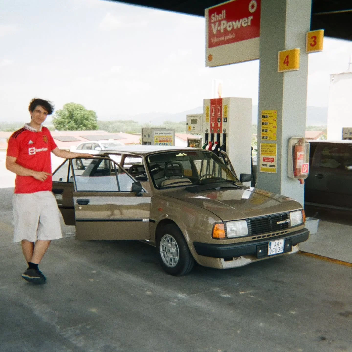 Dominik next to an old Škoda at a petrol station